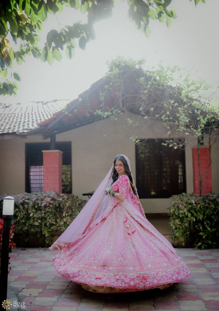 A woman twirling in a pink lehenga outside a cottage