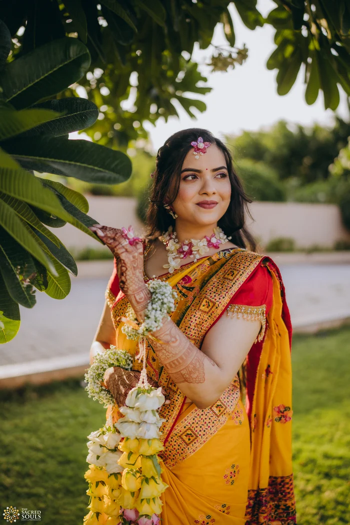 A bride in a yellow Paithani holding a flower garland
