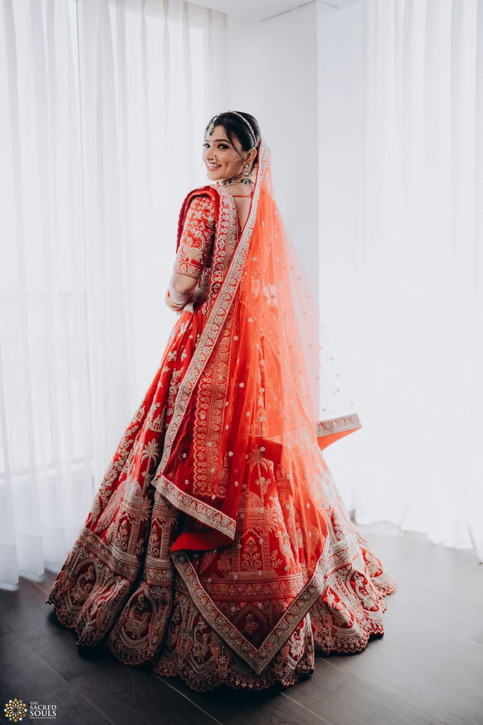 A bride in a red lehenga standing in a bright white room