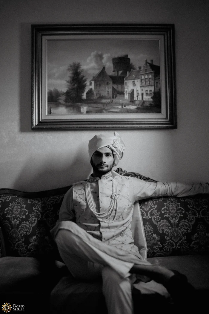 A black-and-white portrait of a groom seated under a painting