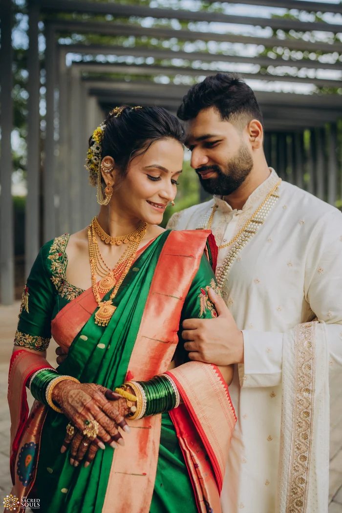 A bride in a green Paithani with her groom under a wooden pergola