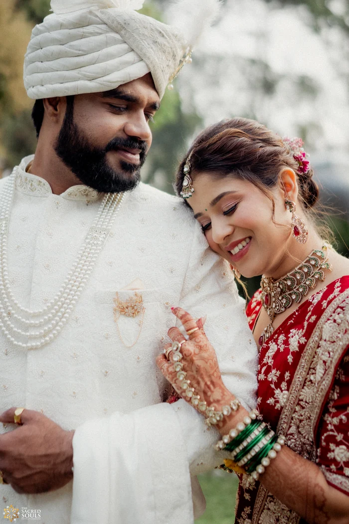 A groom in a white pheta smiling as his bride leans on his shoulder
