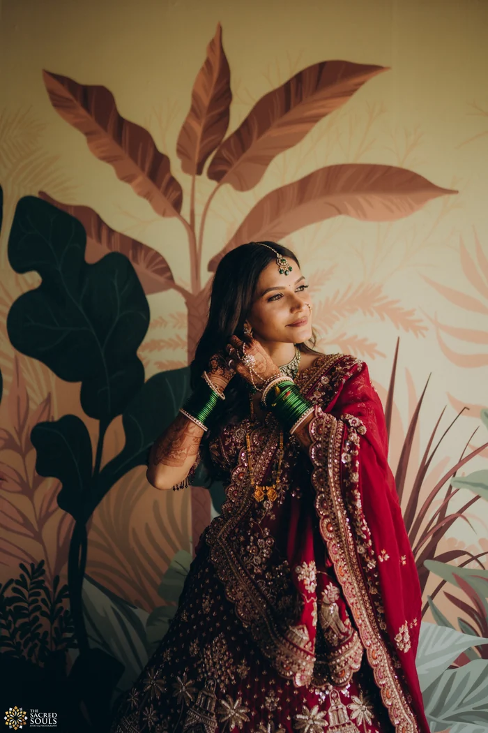 A bride in a lehenga posing against painted leaves