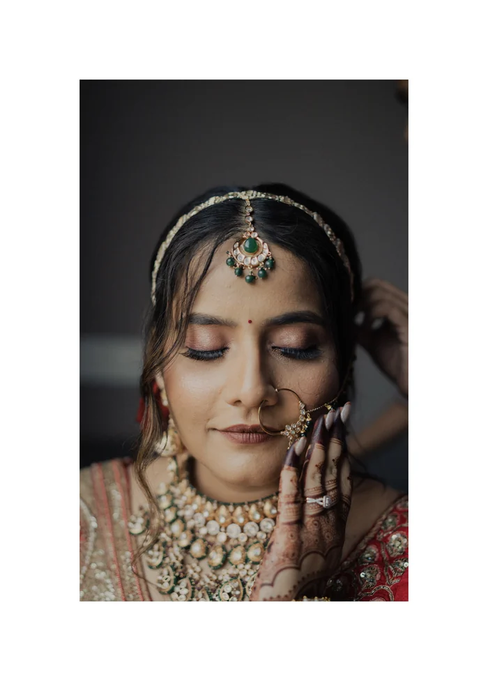 A bride in a maang tikka covering her face with her hand