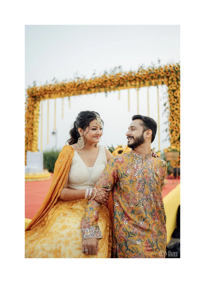 A couple at their haldi under a marigold arch