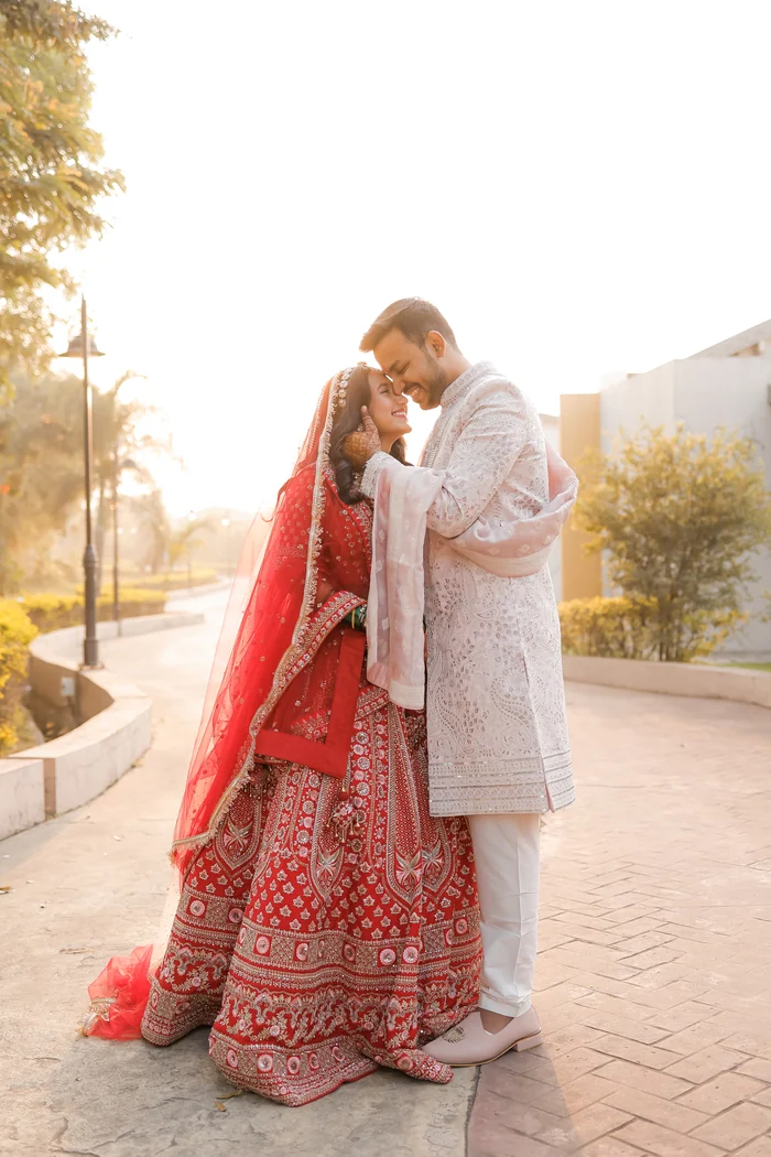 A couple embracing on a sunlit path, she in a red lehenga