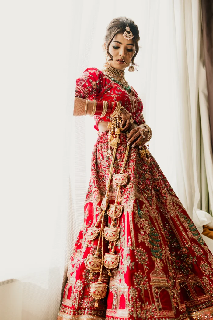 A bride in a red lehenga by a sunlit window